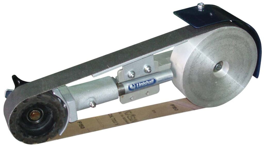 Core Engineering Depot LINISHALL 1220/50 belt grinding attachment on bench grinder with abrasive belt and metal workpiece.